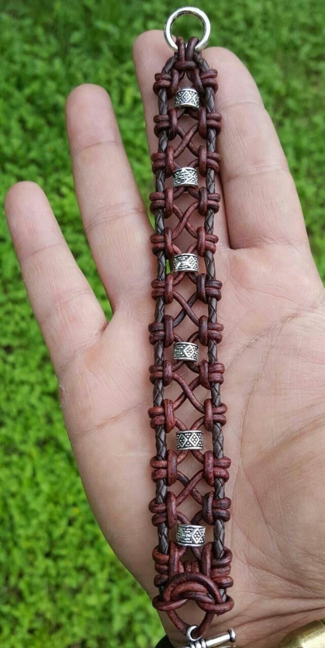 a hand holding a bracelet made out of brown leather and silver metal beads on it's side