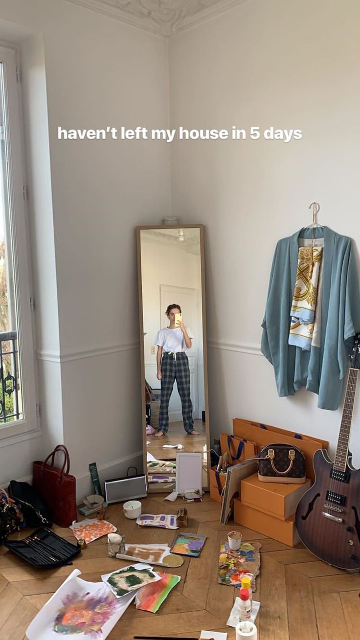 a man standing in front of a mirror next to a table with guitar and other items on it