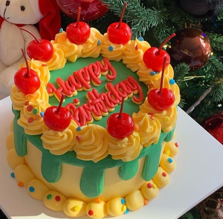 a birthday cake sitting on top of a table next to a teddy bear and christmas tree