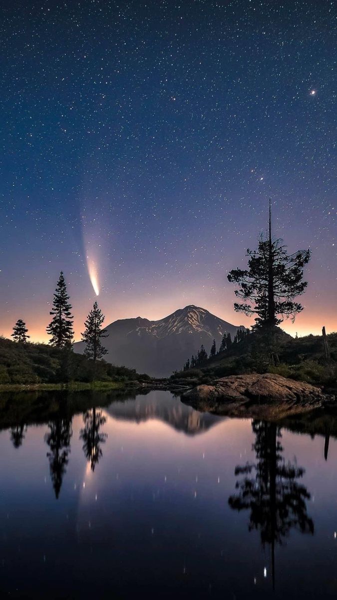 the night sky is reflected in water with trees on both sides and stars above it