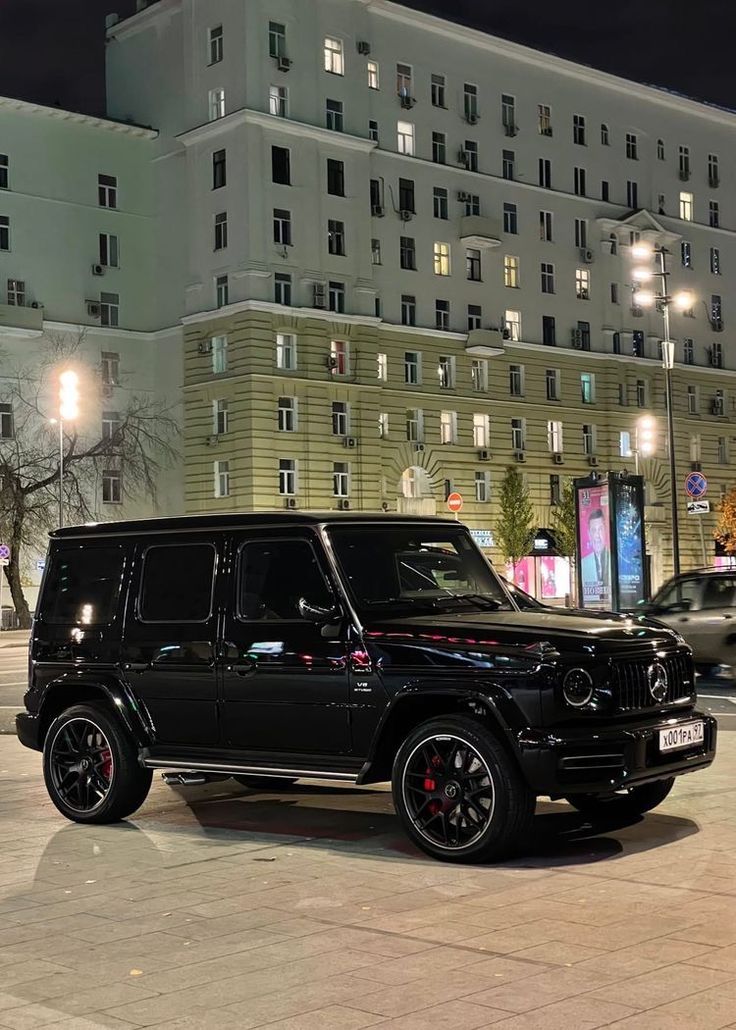 a black suv parked in front of a tall building at night with its lights on