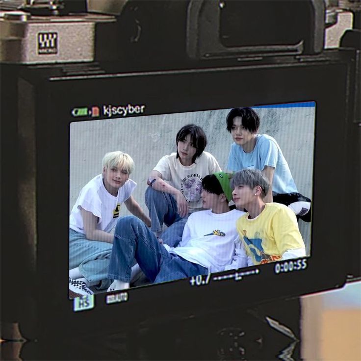 a group of young men sitting on top of a tv screen in front of a camera