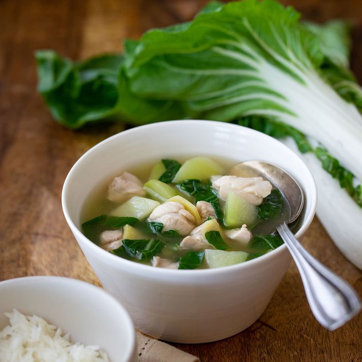 a bowl of chicken and vegetable soup on a wooden table next to some lettuce