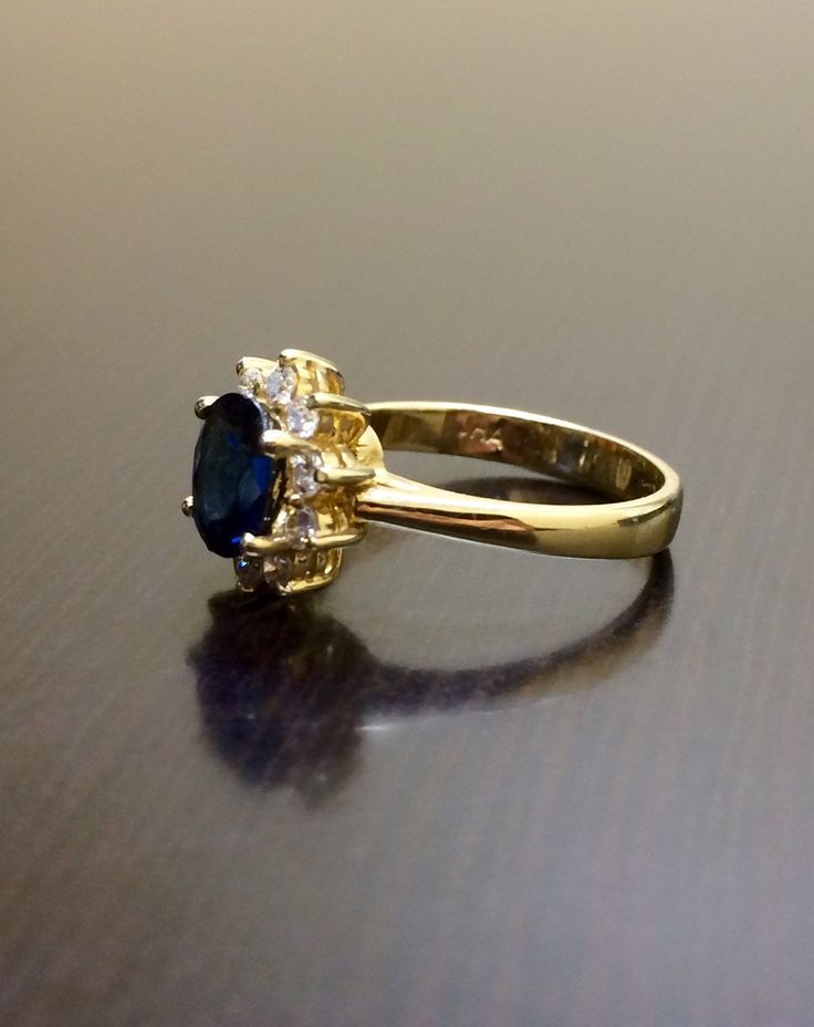 DeKara Designs Collection Metal- 14K Yellow Gold, .583. Stones- 1 Oval Blue Sapphire 1.14 Carats, 10 Round Diamonds G-H Color VS2 Clarity, 0.30 Carats. Size- Ring is a 5 3/4, and could be sized up or down at no additional cost! Handmade 14K Yellow Gold Sapphire and Diamond Ring. This ring is inspired by the Art Deco era with an enticing fiery oval shaped blue sapphire. The sapphire is set in between 4 prongs. The sapphire has a halo of prong set 10 round diamonds surrounding them which brings ou Sapphire Diamond Wedding Ring, Sapphire Diamond Engagement Ring, Diamond Sapphire Engagement Ring, Sapphire Diamond Engagement, Sapphire And Diamond Ring, Ring Halo, Blue Sapphire Diamond, Gold Halo, Diamond Wedding Ring