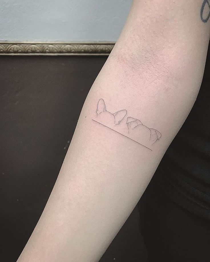 a woman's arm with a small tattoo of three cats on the left forearm