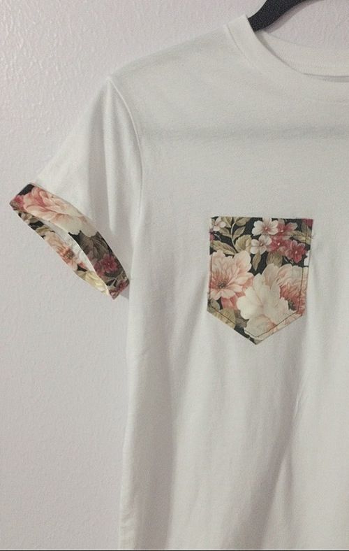 a white t - shirt with floral pocket on the front and back, hanging from a hanger