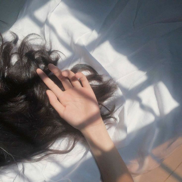 a woman laying on top of a bed holding her hand up to her head and touching her hair