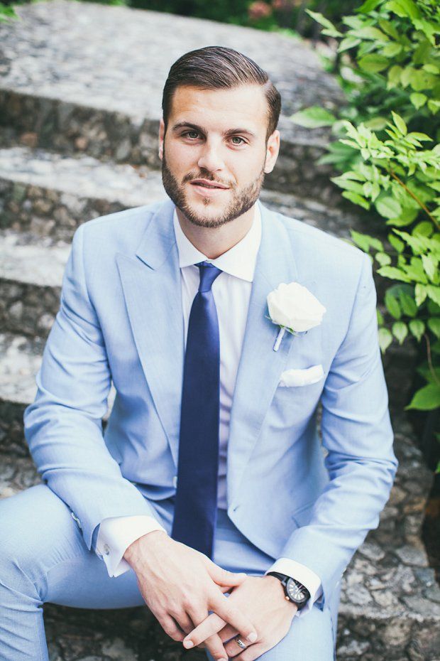 a man in a blue suit sitting on some steps with a white rose pinned to his lapel