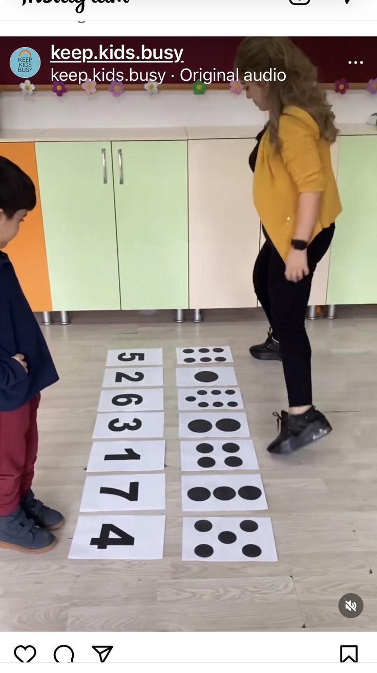 two young children playing with numbers on the floor in a kitchen, and one child is standing next to them