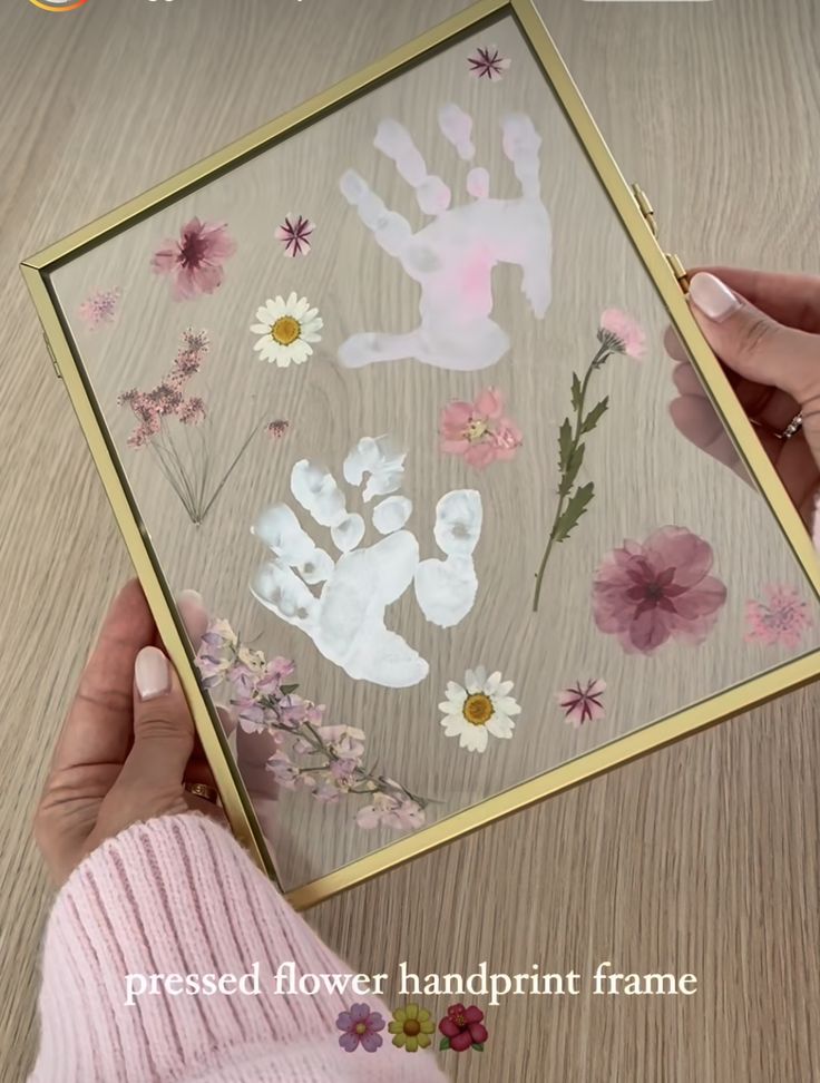 a person is holding up a handprint frame with flowers on it and the words pressed flower handprint frame