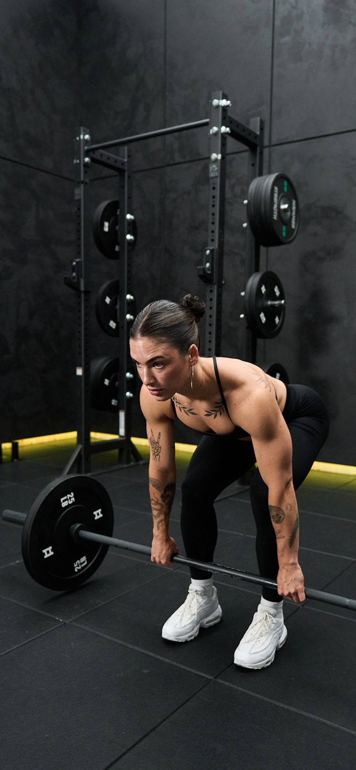 a woman squatting down with a barbell in her hand and looking at the camera