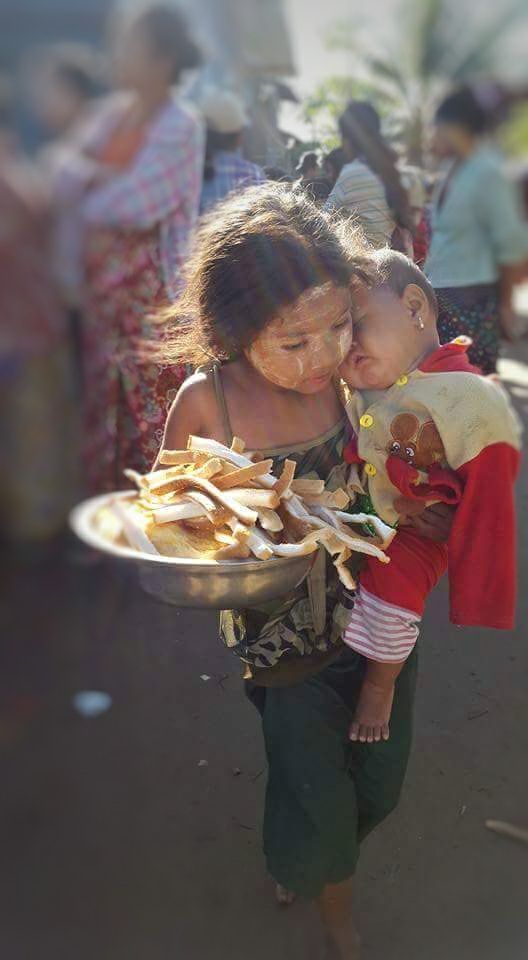 a woman carrying a child on her back in front of other people and eating food