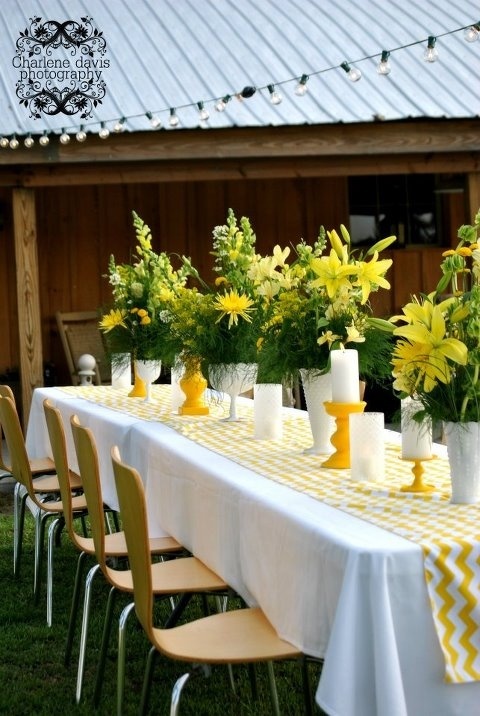 a long table with yellow and white flowers in vases sitting on top of it