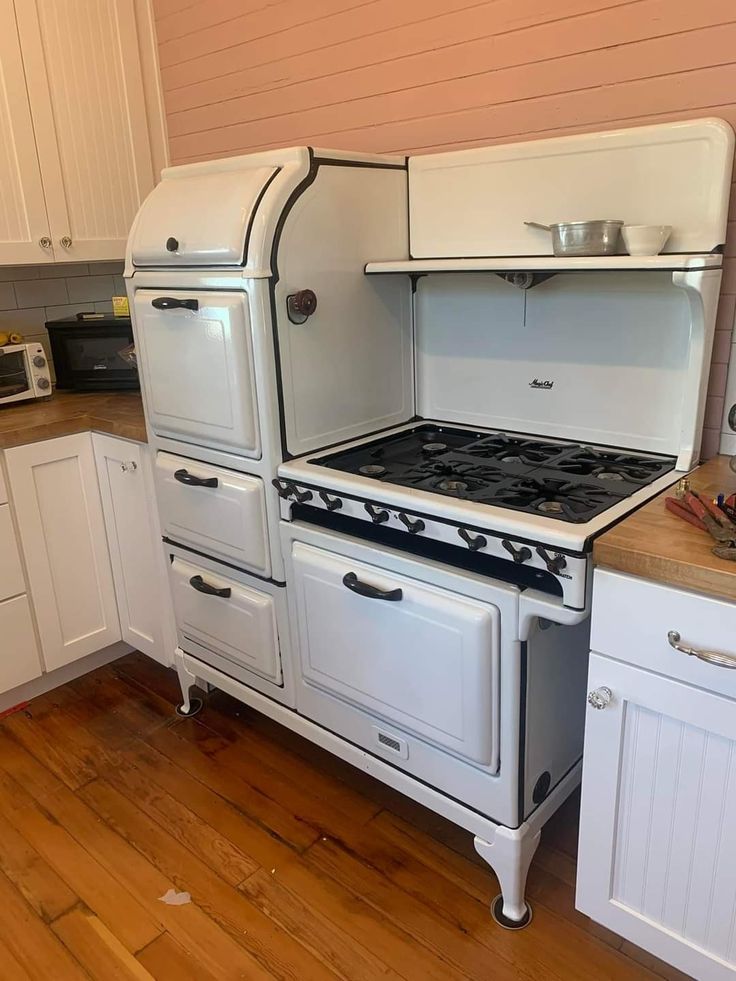 an old fashioned stove in the middle of a kitchen with white cabinets and wood floors