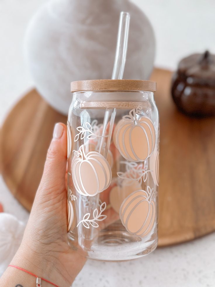 a person holding a glass jar with pumpkins on it and a donut in the background