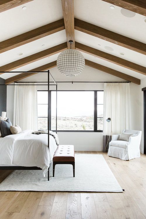 a bedroom with white bedding and wooden beams on the ceiling, along with a large window