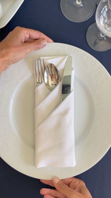 two hands are holding silverware on a white plate with napkins and wine glasses