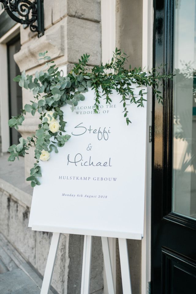 a white sign with greenery on it in front of a building