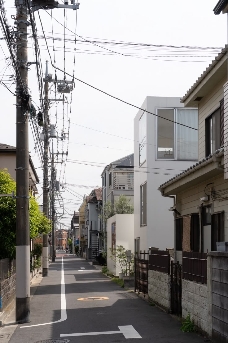 an empty street with power lines above it and houses on the other side, along with telephone poles