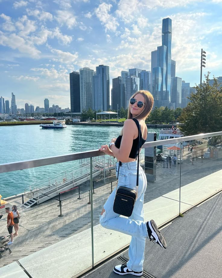 a woman is standing on the edge of a railing looking at the water and buildings in the background