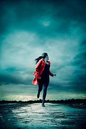 a woman is running on the beach under a cloudy sky