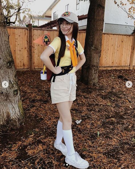 a woman is standing in front of a tree wearing white boots and a yellow shirt