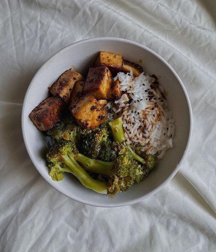 a bowl filled with rice, broccoli and tofu on top of a bed