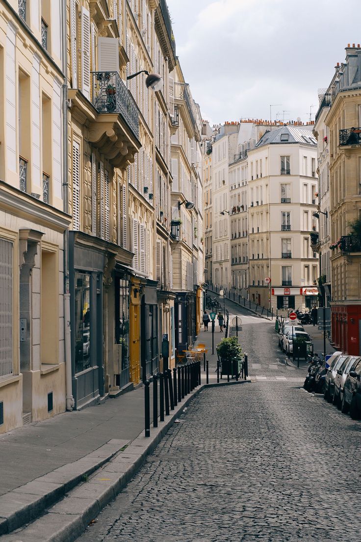 an empty cobblestone street lined with buildings and parked cars in paris, france