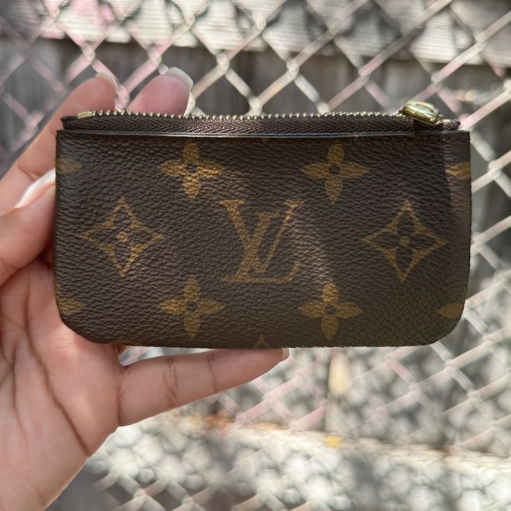 a hand holding a small brown purse with gold letters on the front and bottom half