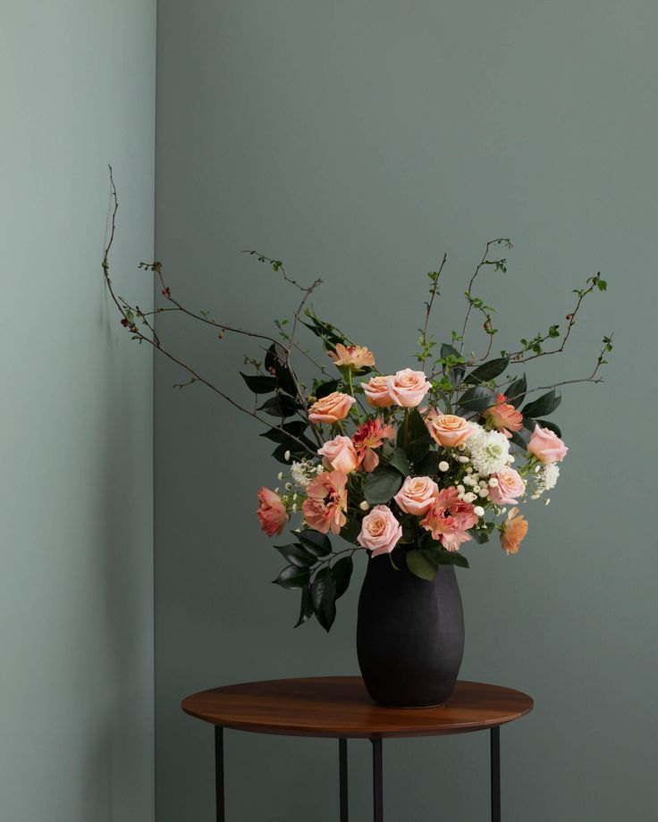 a black vase filled with pink and white flowers on top of a small wooden table