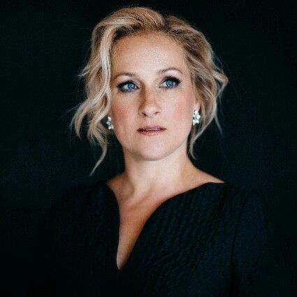 a woman with blonde hair and blue eyes looking at the camera while wearing black dress