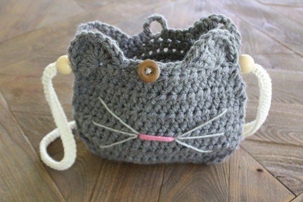 a crocheted gray cat purse sitting on top of a wooden floor