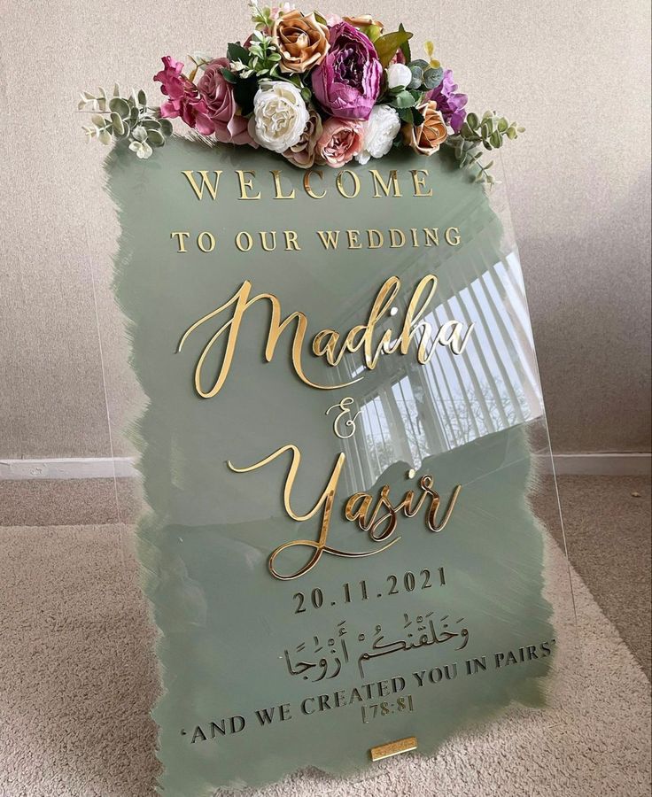 a welcome sign with flowers on it in front of a white wall and carpeted floor