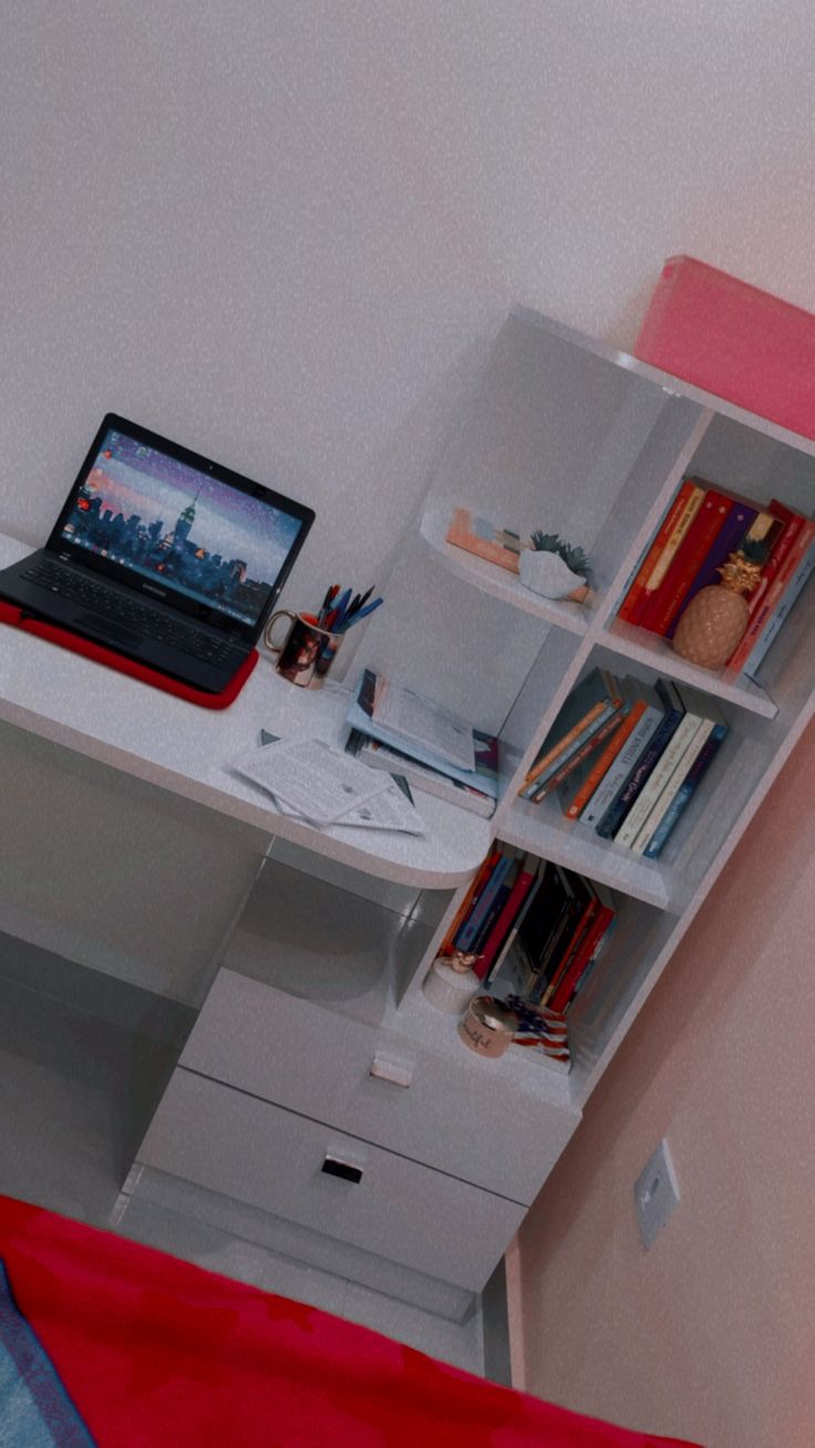 a laptop computer sitting on top of a white desk next to a book shelf filled with books