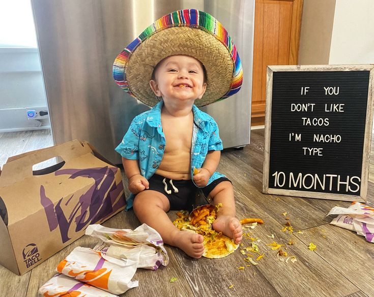 a baby wearing a sombrero sitting on the floor next to a sign that says, if you don't like tacos i'm nacho type 10 months