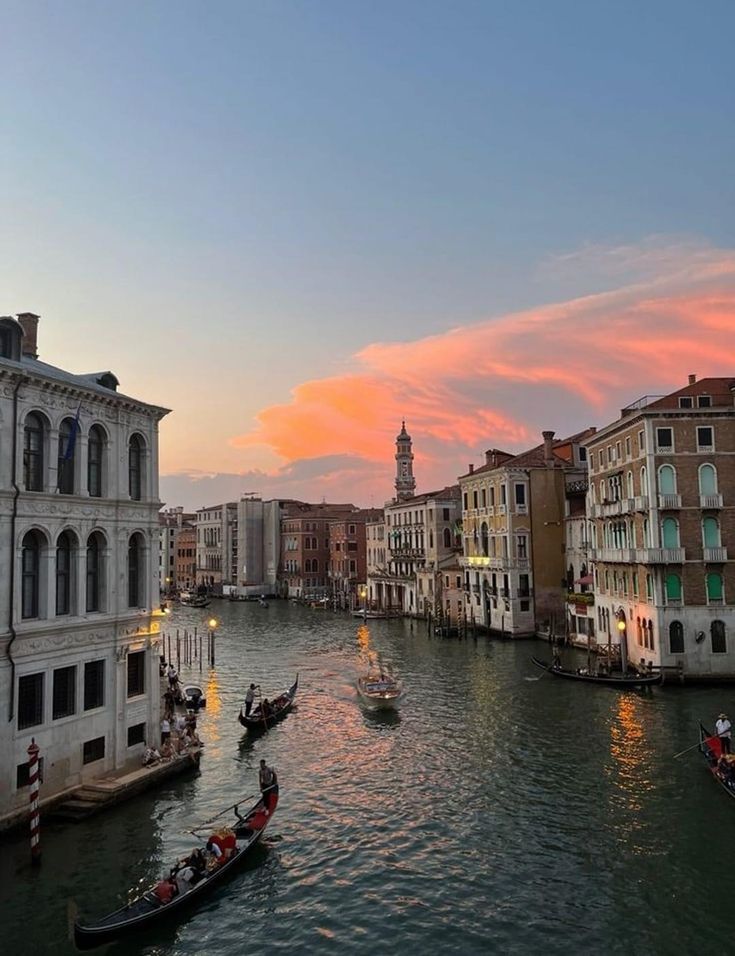 several gondolas are on the water in front of some buildings and lights at sunset