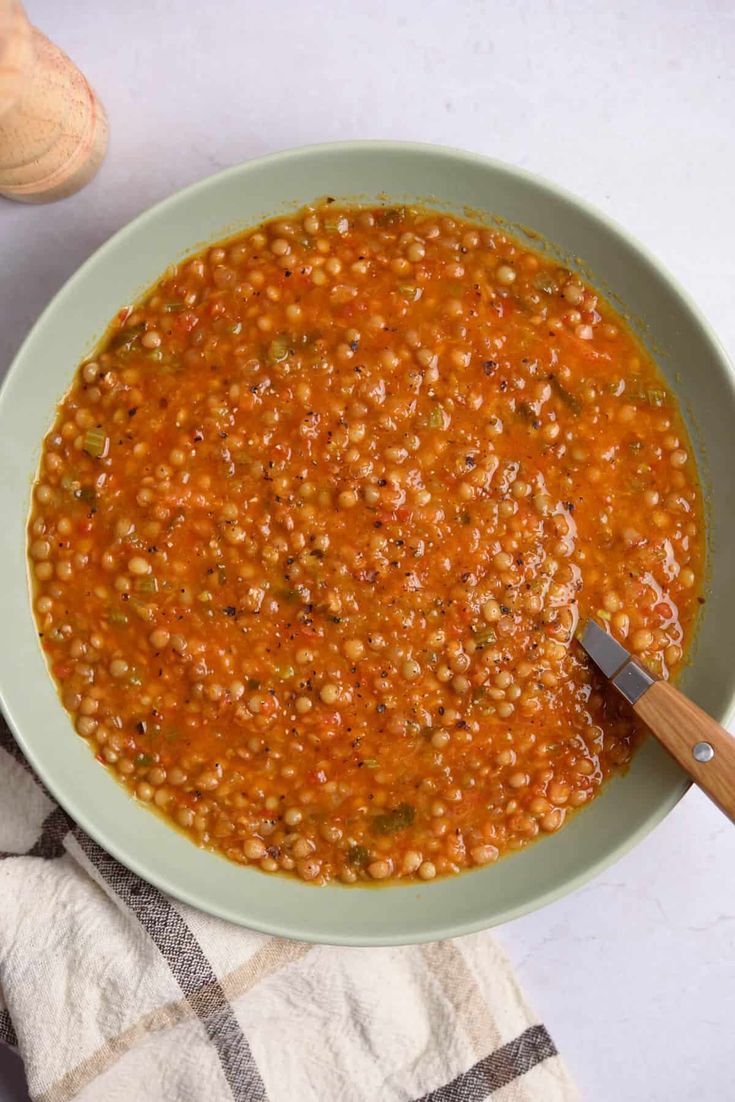 a white bowl filled with red lentula soup on top of a checkered table cloth