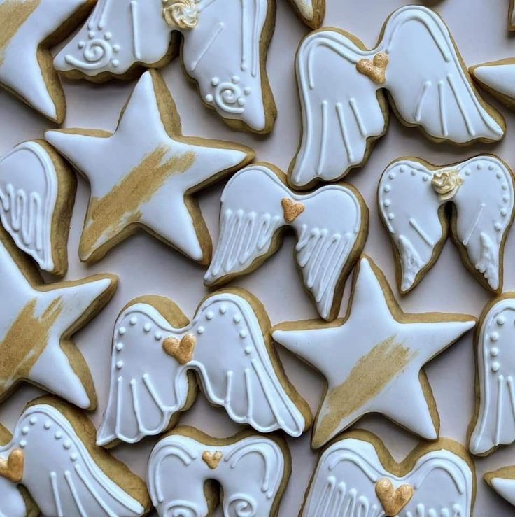 many decorated cookies in white and gold with angel wings, hearts, and stars on them