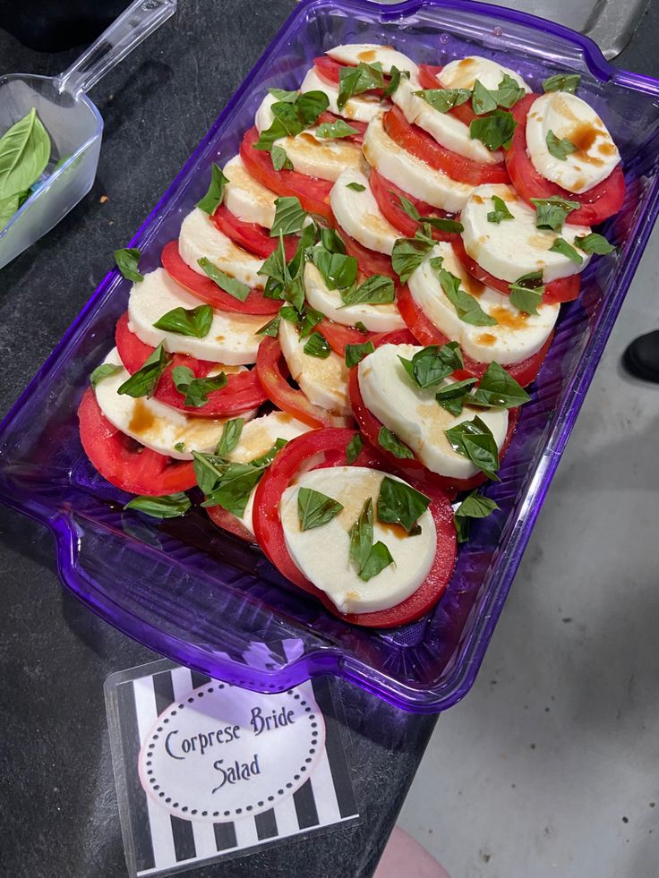 a purple container filled with sliced tomatoes and mozzarella on top of a table