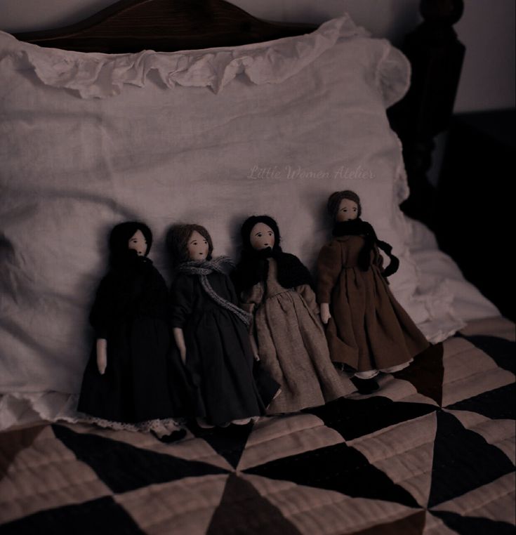 four dolls are sitting on top of a bed