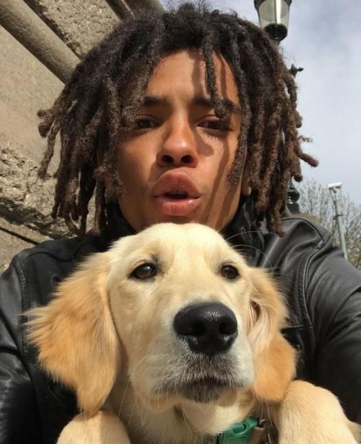 a man with dreadlocks holding a dog in front of his face and looking at the camera