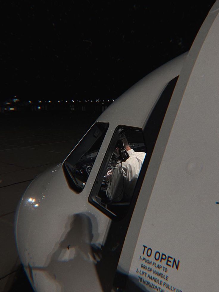 a man sitting in the cockpit of an airplane at night with his feet out the window