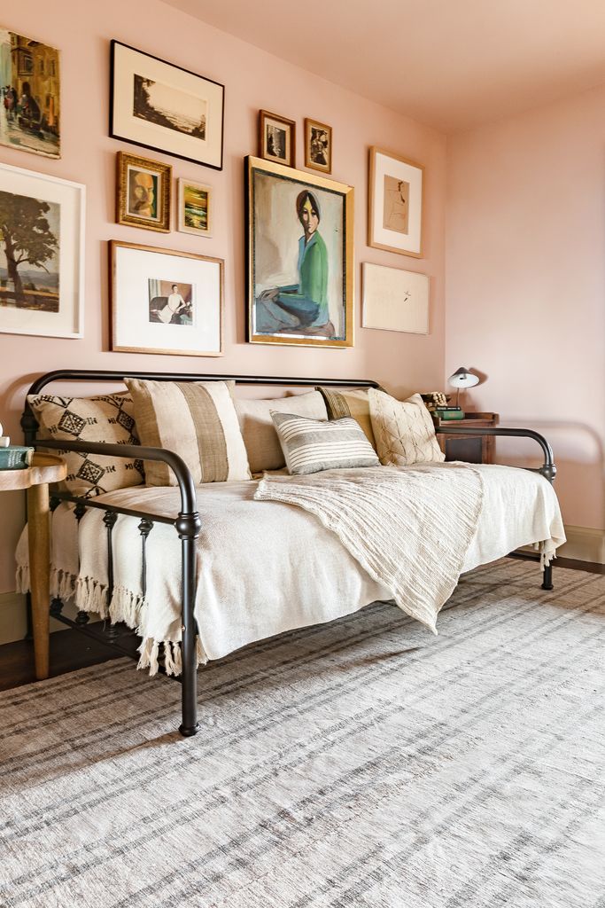 a living room with pink walls and pictures on the wall above the couch, along with an area rug