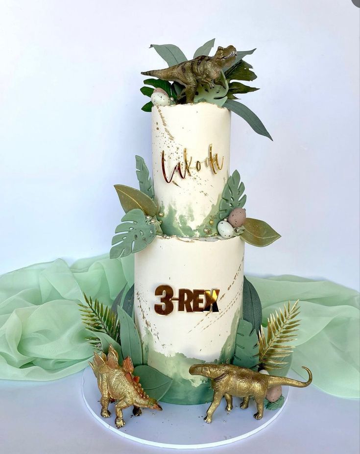 a three tiered cake with dinosaur figurines on the side and greenery around it