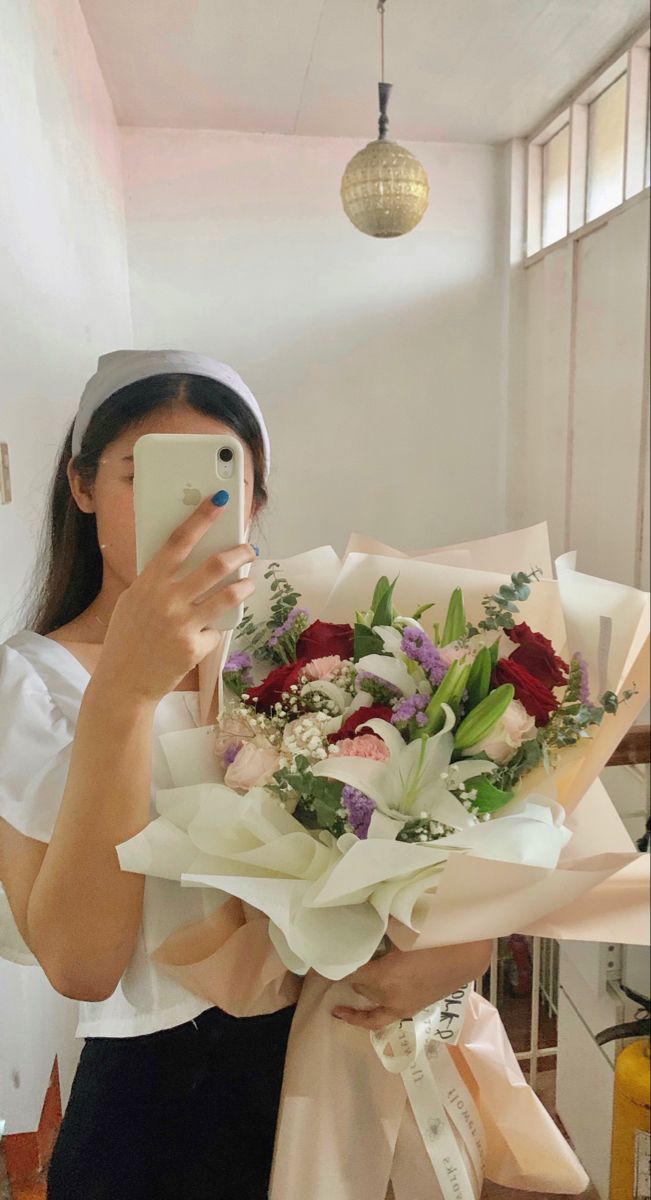 a woman taking a selfie with flowers in front of her face while holding a cell phone