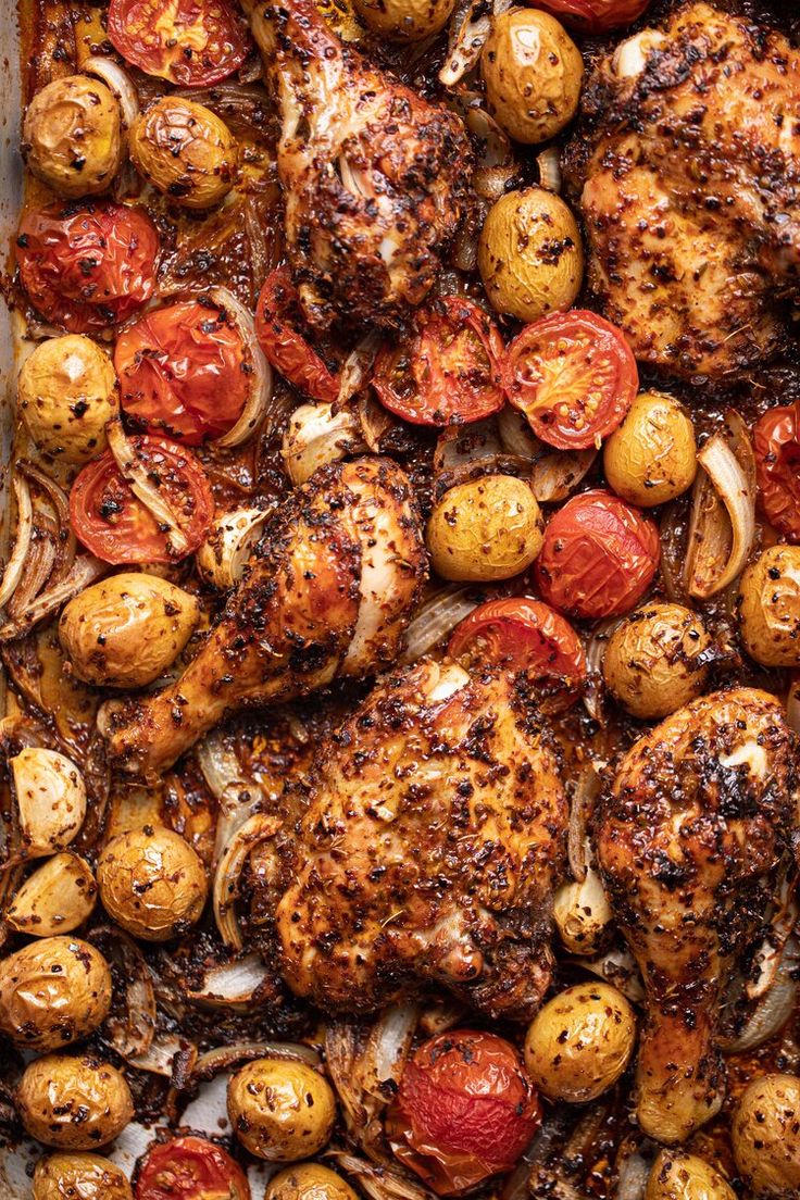 chicken, potatoes and tomatoes on a sheet pan with seasoning sprinkled over them