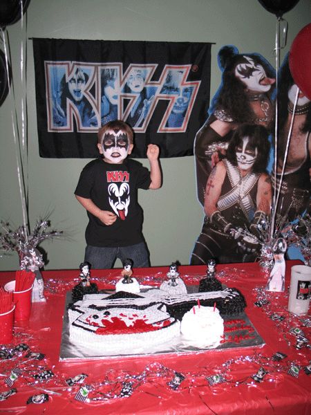 a young boy standing in front of a cake on top of a red table cloth