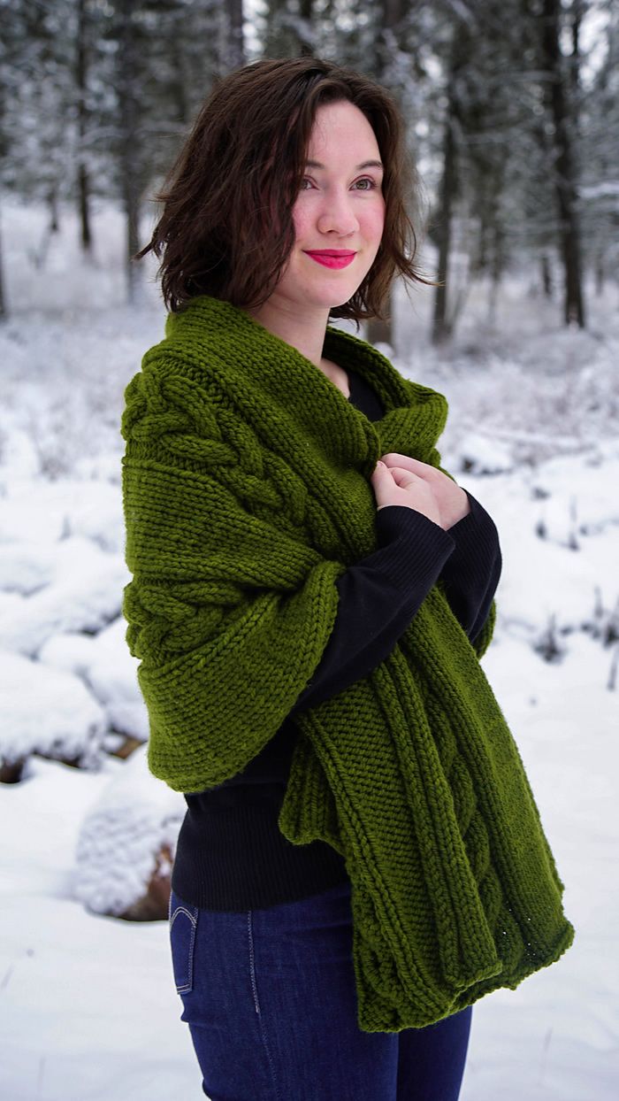 a woman standing outside in the snow wearing a green knitted shawl over her shoulders