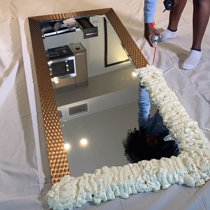 a person is painting a large mirror with white frosting on the bottom and gold trim around it