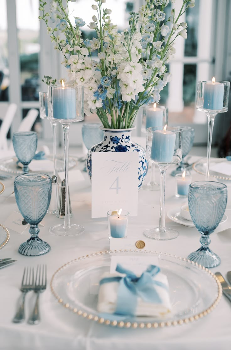 the table is set with blue and white dishes, silverware, candles, and flowers